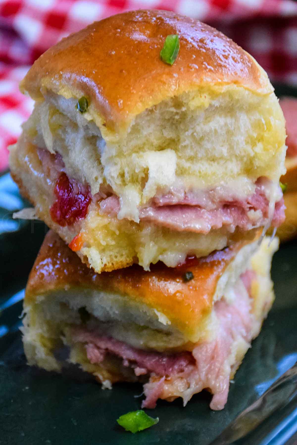 Ham and cheese sliders stacked with melted cheese, ham, and pepper jelly on soft rolls.