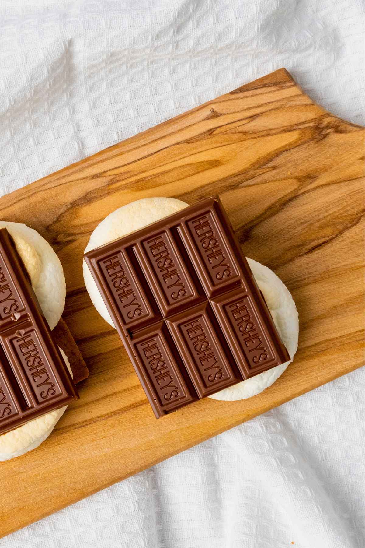 Two graham cracker halves topped with hershey's milk chocolate and toasted marshmallows on a wooden board.