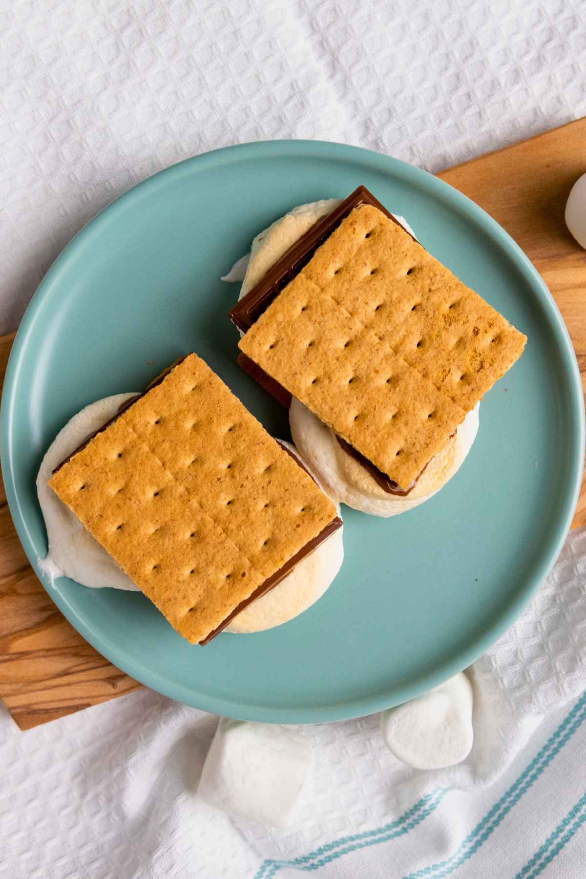 Two Air Fryer S'mores made with toasted marshmallows, milk chocolate, and graham crackers on a teal plate.