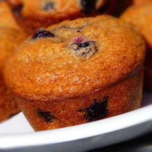 A batch of golden brown Blueberry Apple Butter Muffins with a slighty glossy top, studded wth baked blueberries, resting in a white dish.
