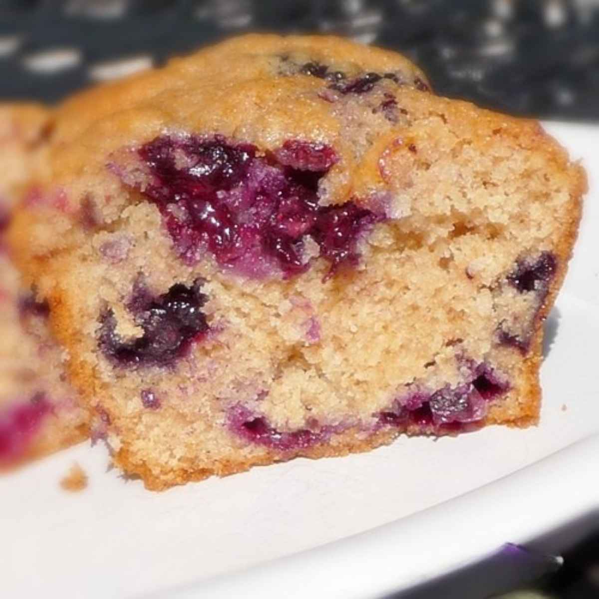 A close-up of a blueberry muffin sliced in half, showing its moist, golden crumb with juicy purple blueberries throughout.