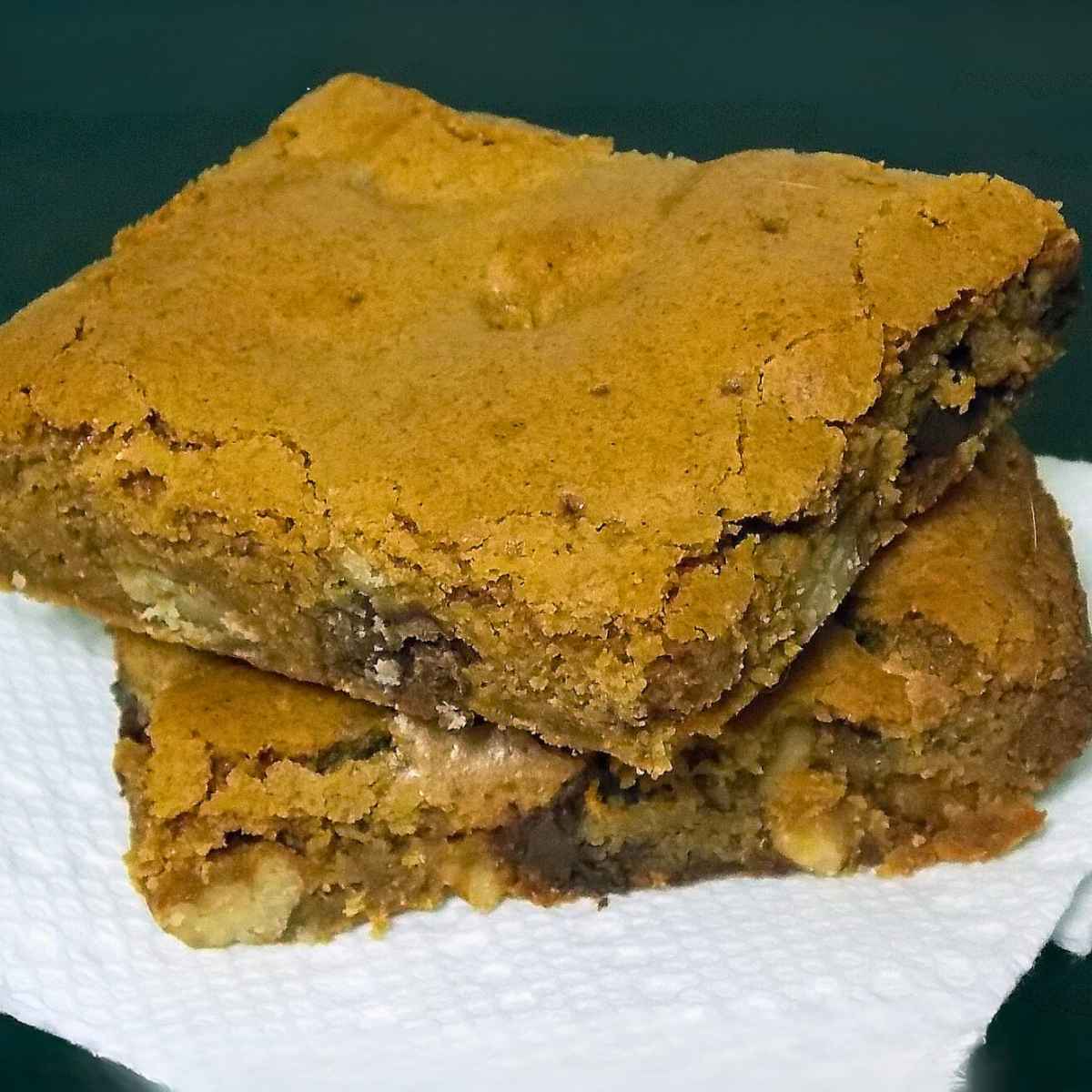 Two golden brown bourbon chocolate chip blondies stacked on a white napkin, showing a soft, chewy texture with visible chocolate chips and nuts.