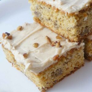 A stack of banana bars with brown butter frosting and topped with chopped pecans.