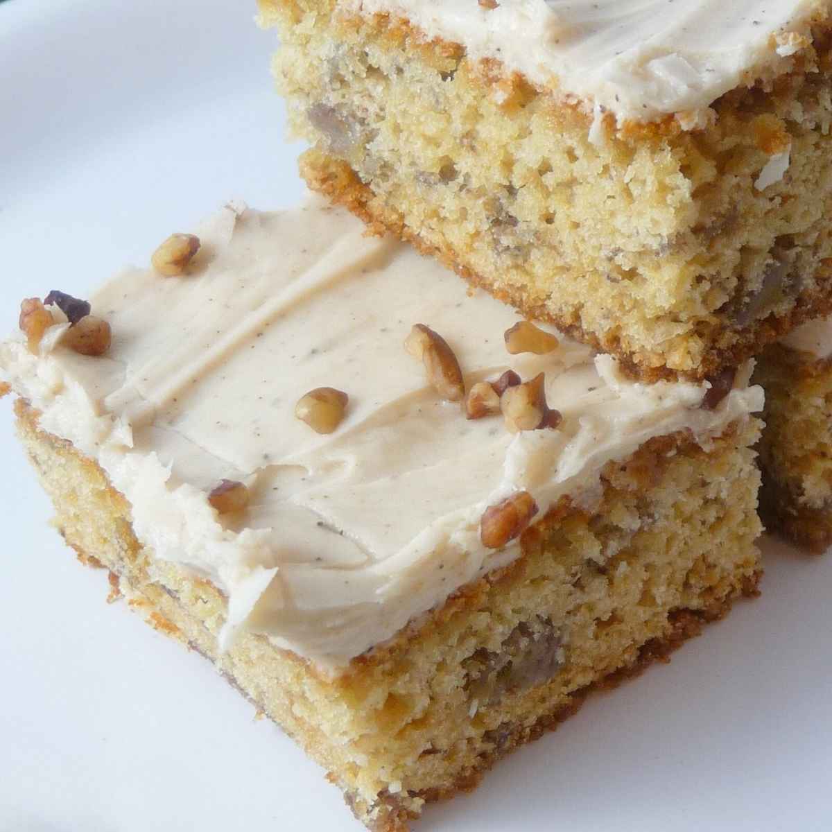 A stack of banana bars with brown butter frosting and topped with chopped pecans.