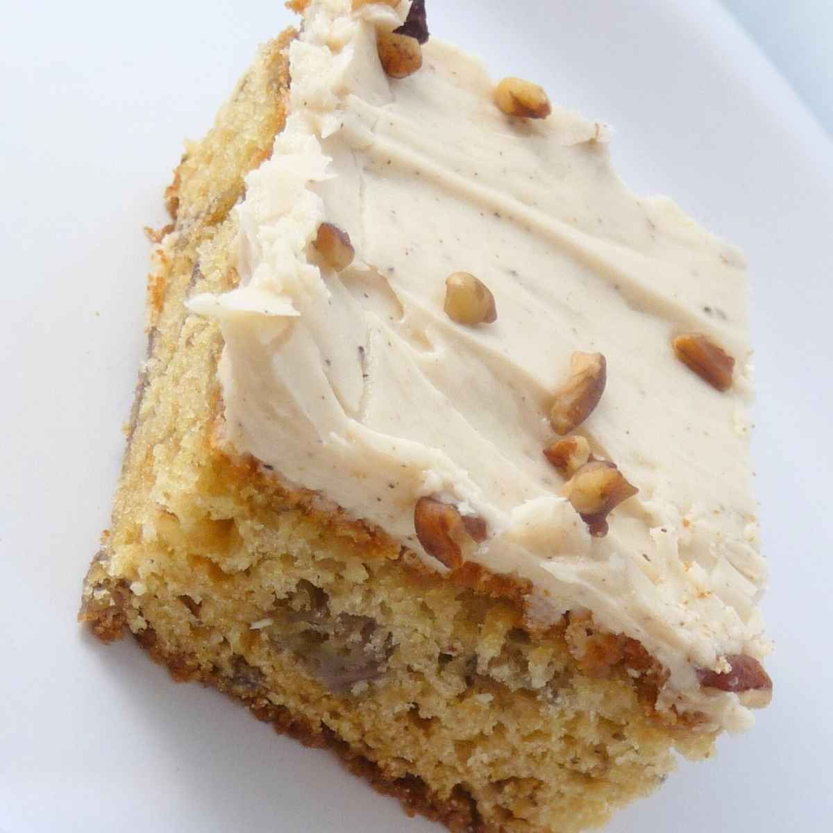 Close up of two frosted brown butter banana bars stacked on a white plate, topped with creamy brown butter frosting and small pieces of chopped nuts.