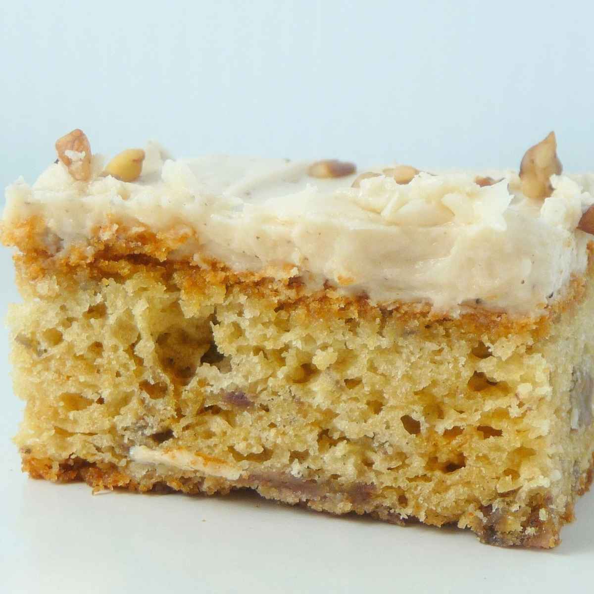 A side view of a banana bar frosted with brown butter cream cheese frosting and topped with chopped pecans.