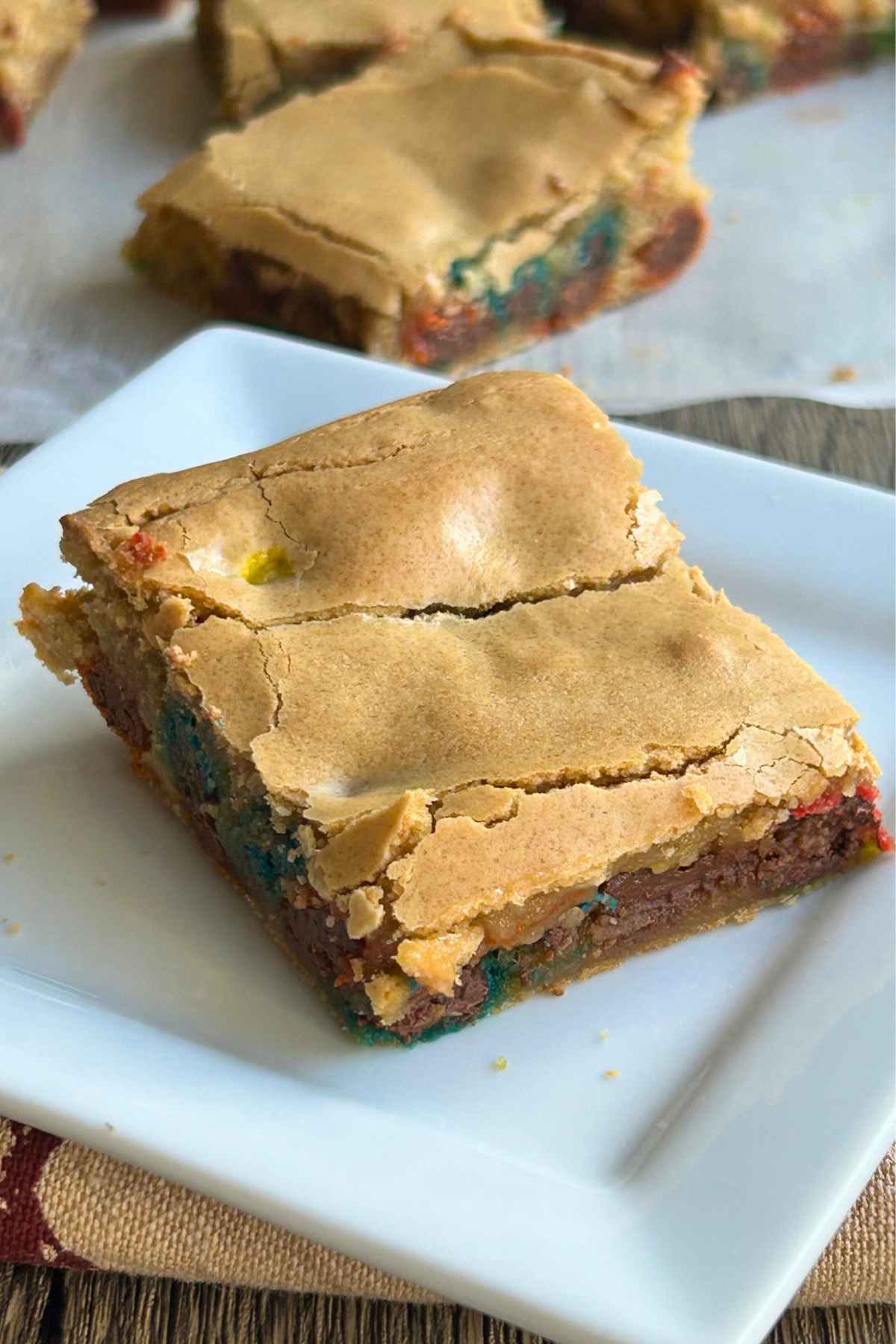 A single blondie square on a white plate with a cracked golden top and colorful candies visible on the inside.
