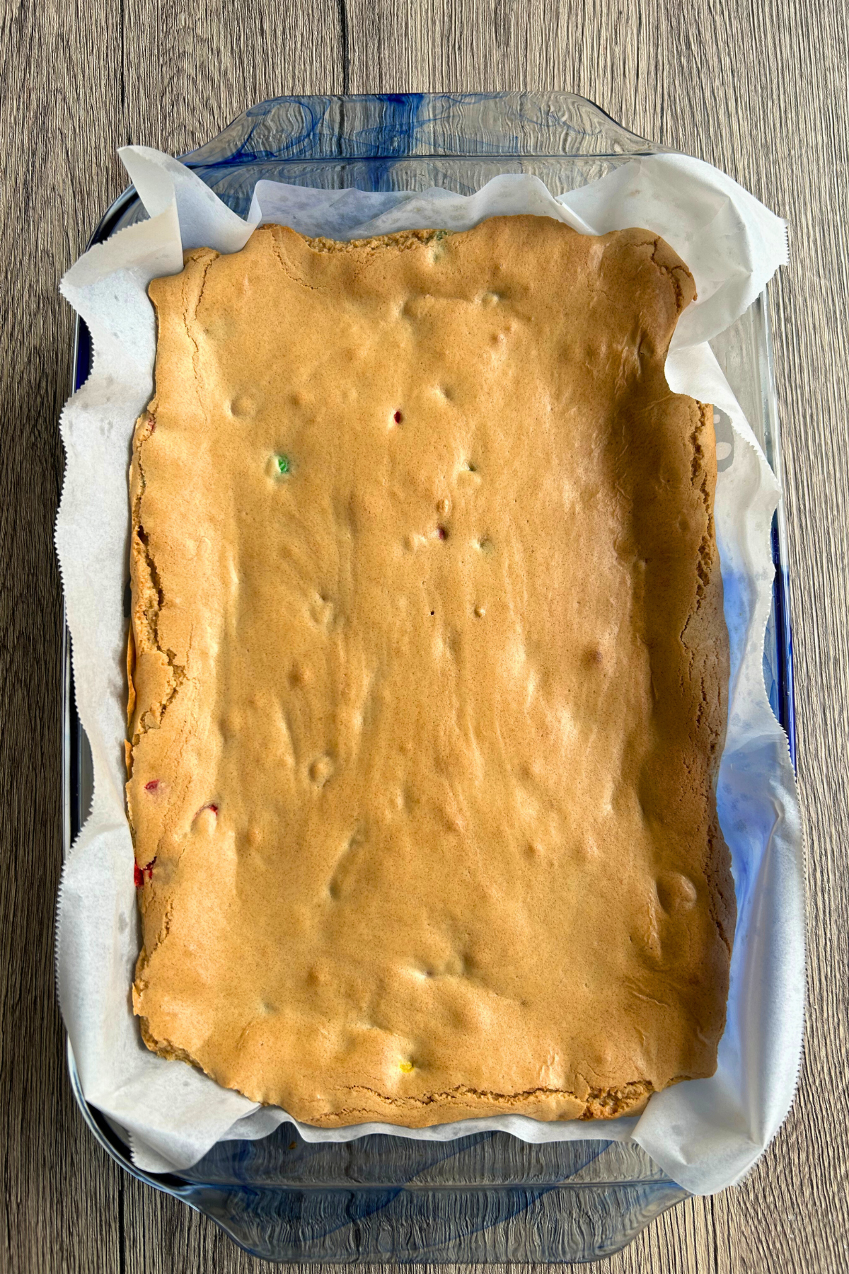 Overhead view of a pan of freshly baked brown butter blondie bars lined with parchment paper, showing a smooth golden-brown surface.