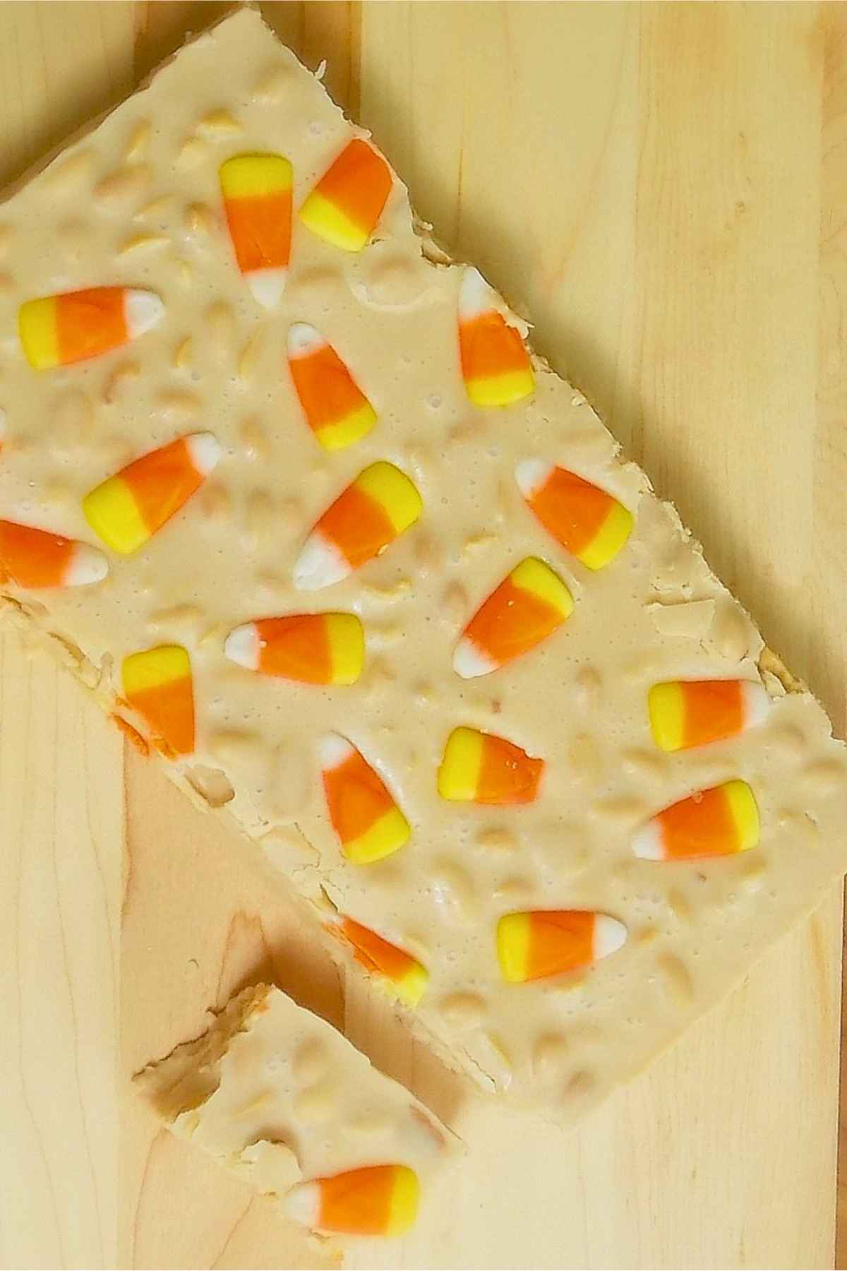 Overhead view of a rectangular slab of candy corn fudge pieces on a wooden board with one corner piece cut away.