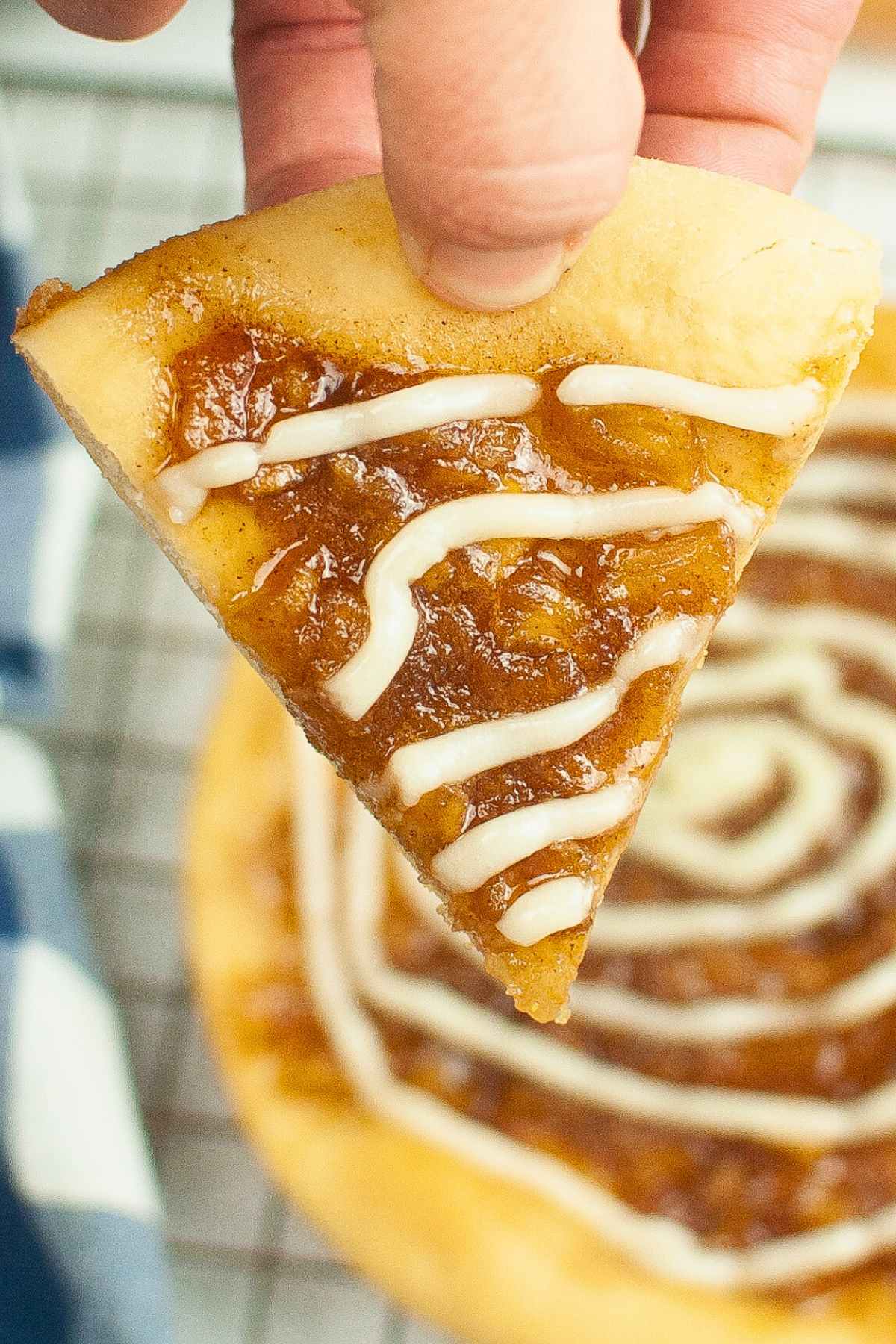 One triangular cut piece of caramel apple pizza being held by a hand.