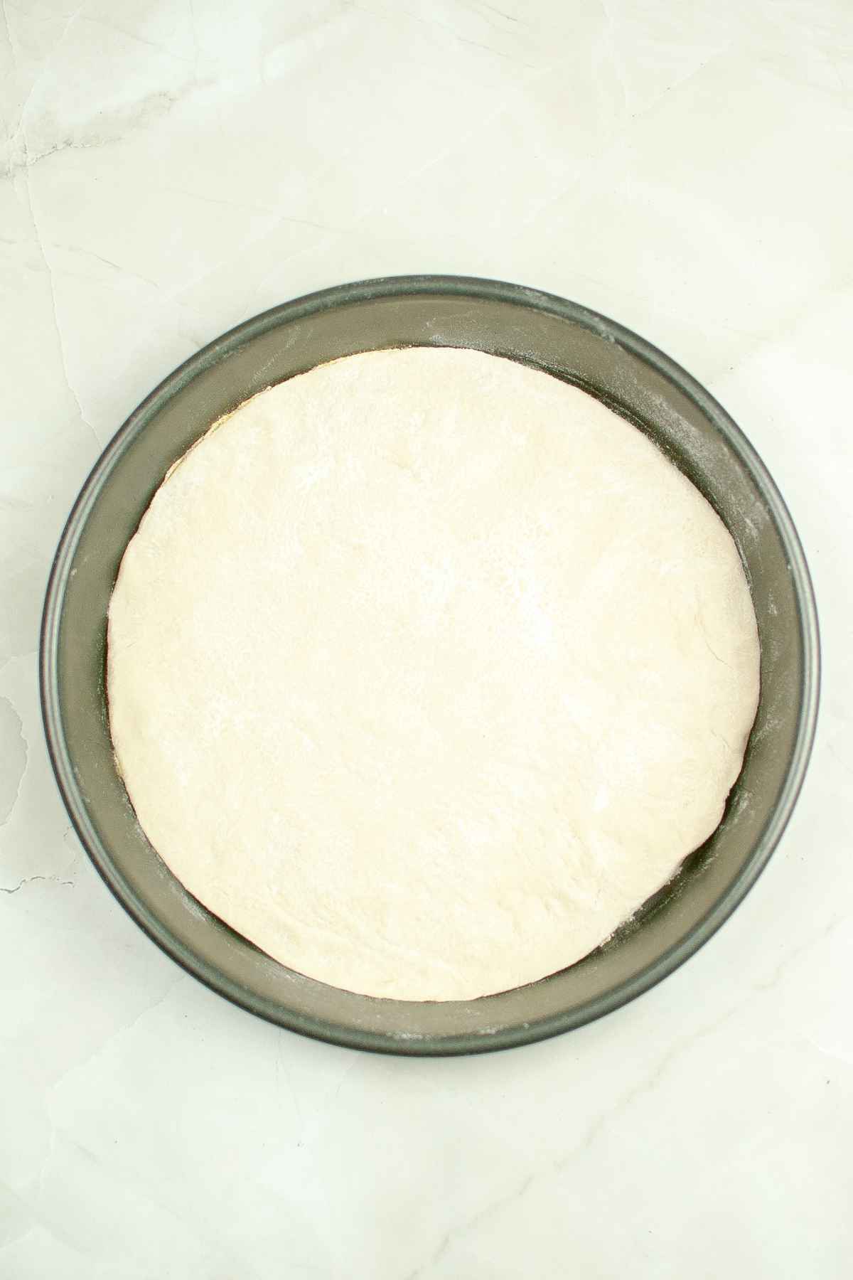 A round pan with a smooth layer of rolled out pizza dough ready for pre-baking.