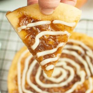 One triangular cut piece of caramel apple pizza being held by a hand.