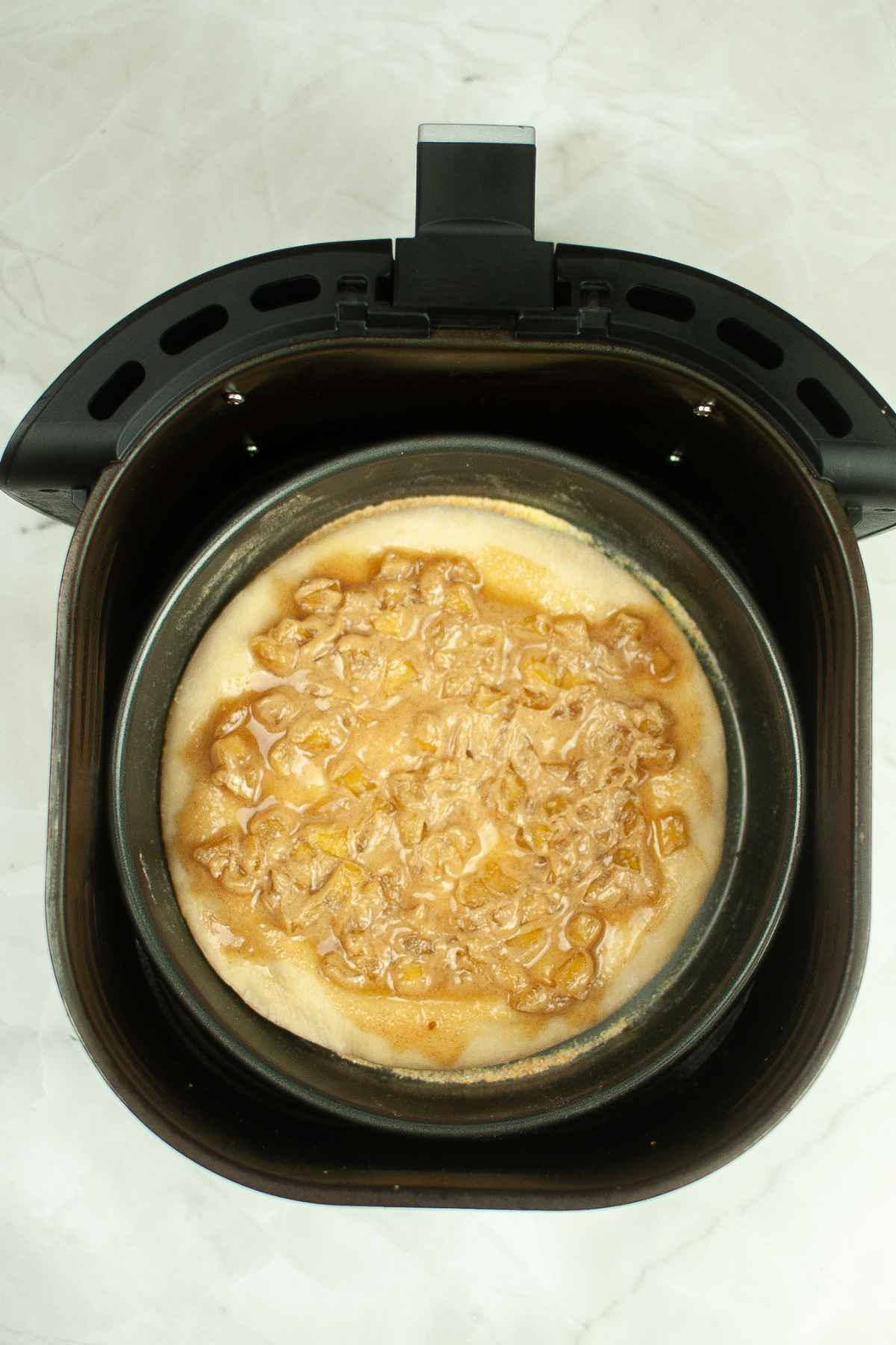 A pan filled with caramel apple topping over dough placed inside an air fryer basket before baking.