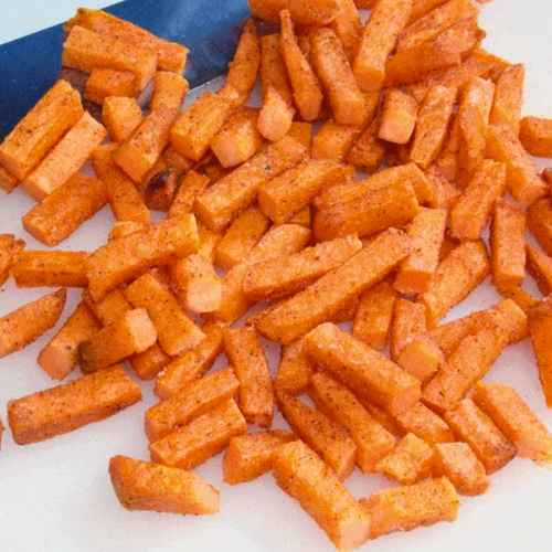 Seasoned sweet potato fries cut into short strips, spread across a cutting board.
