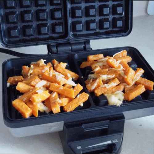 A waffle maker filled with sweet potato fries and shredded cheese before cooking.