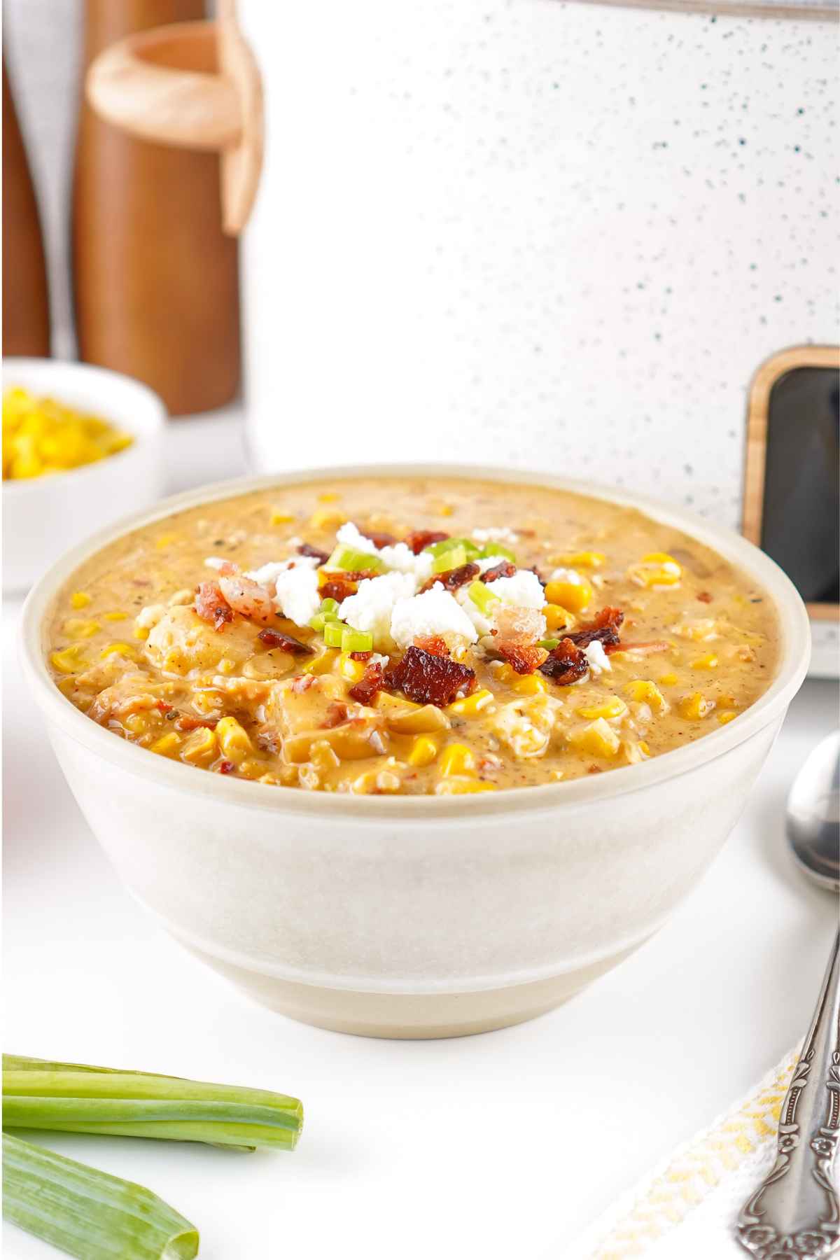 Bowl of mexican street corn soup toped with bacon, crumbled cheese, and sliced green onions.