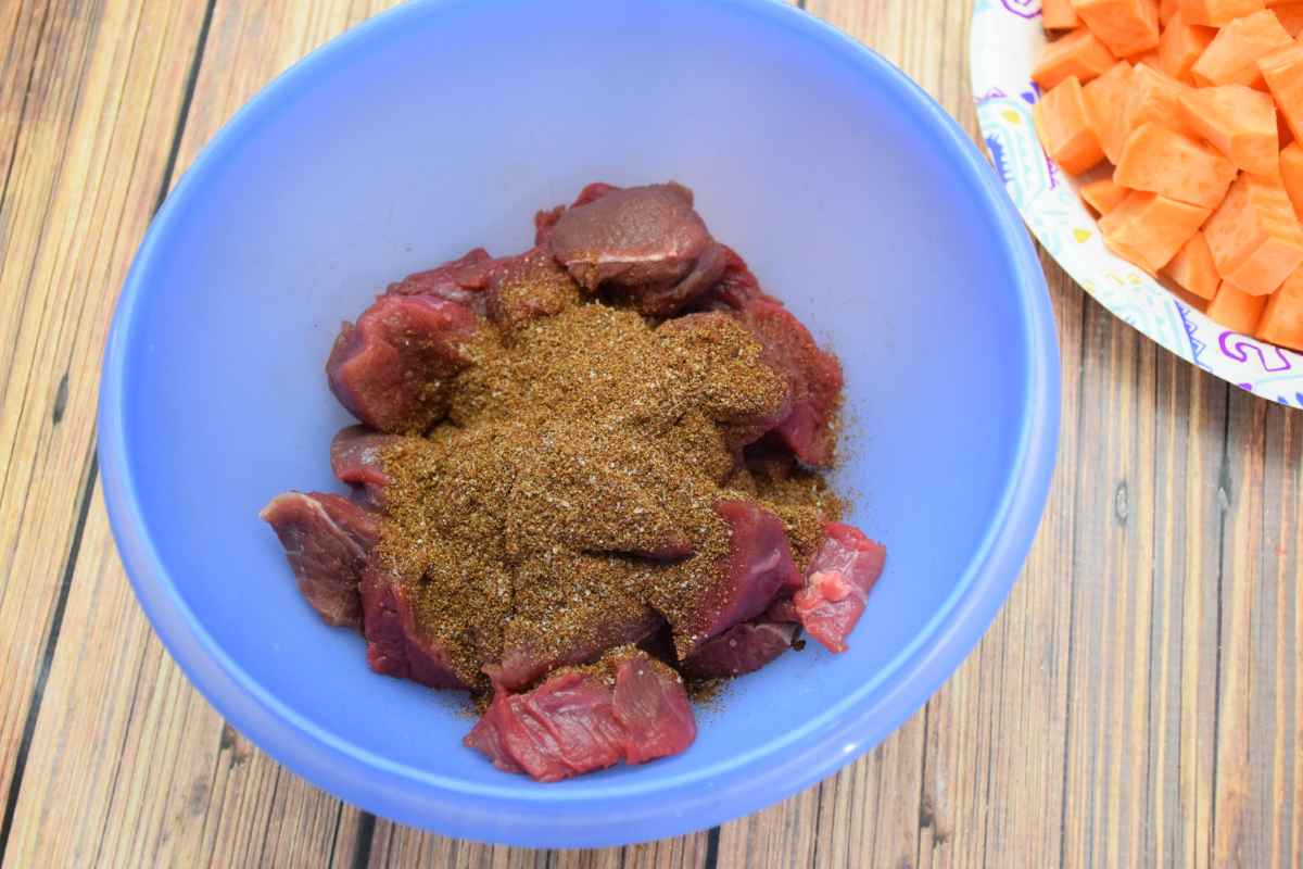 Cubed venison in a blue bowl topped with a generous amount of dark seasoning blend.