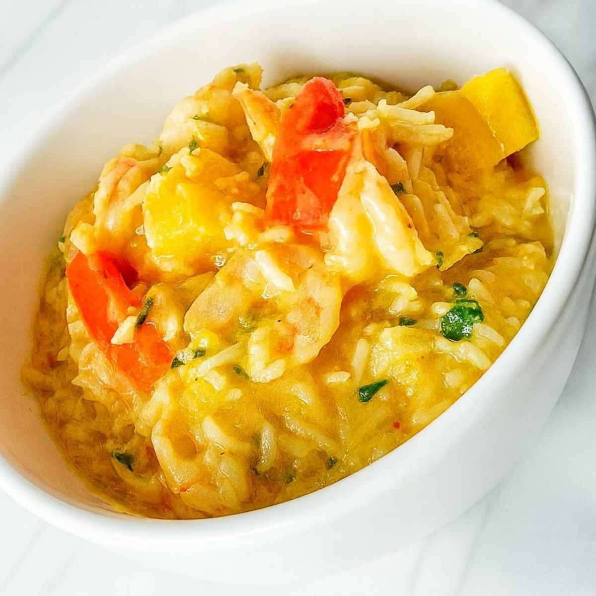 A white bowl filled with butternut squash coconut shrimp curry showing pieces of rice, squash, red bell pepper, and shrimp.