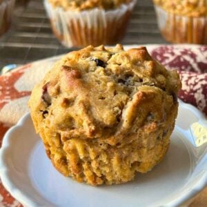 Upclose image of Cranberry All Bran Muffins on a white plate with leaf prpinted napkin.