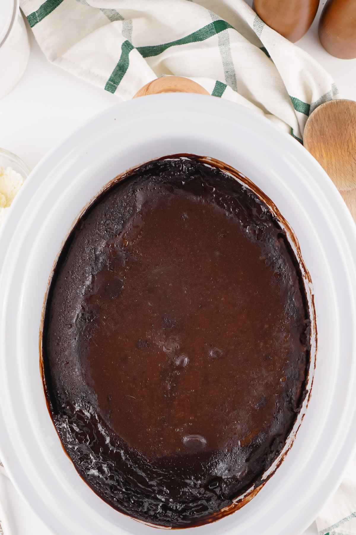 A freshly baked chocolate cobbler in a white oval slow cooker, showing a rich, glossy layer of melted chocolate on top.
