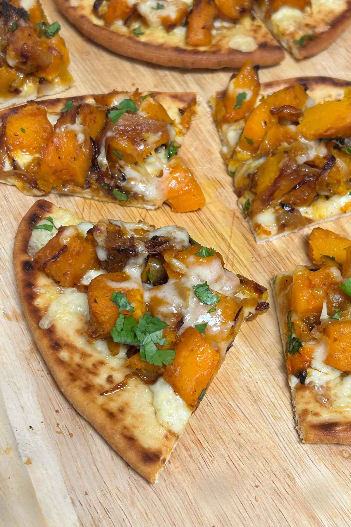 Slices of curried roasted butternut squash, caramelized onions, melted cheese, and fresh herbs on a wooden board.