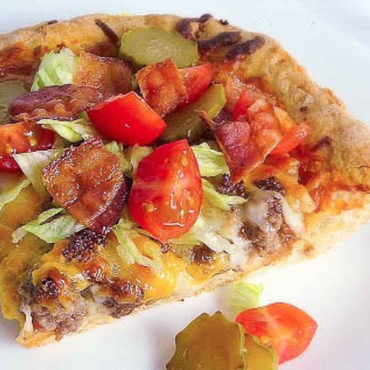 A slice of pizza with melted cheese, crispy bacon, lettuce, tomato, and pickle slices on a golden crust.