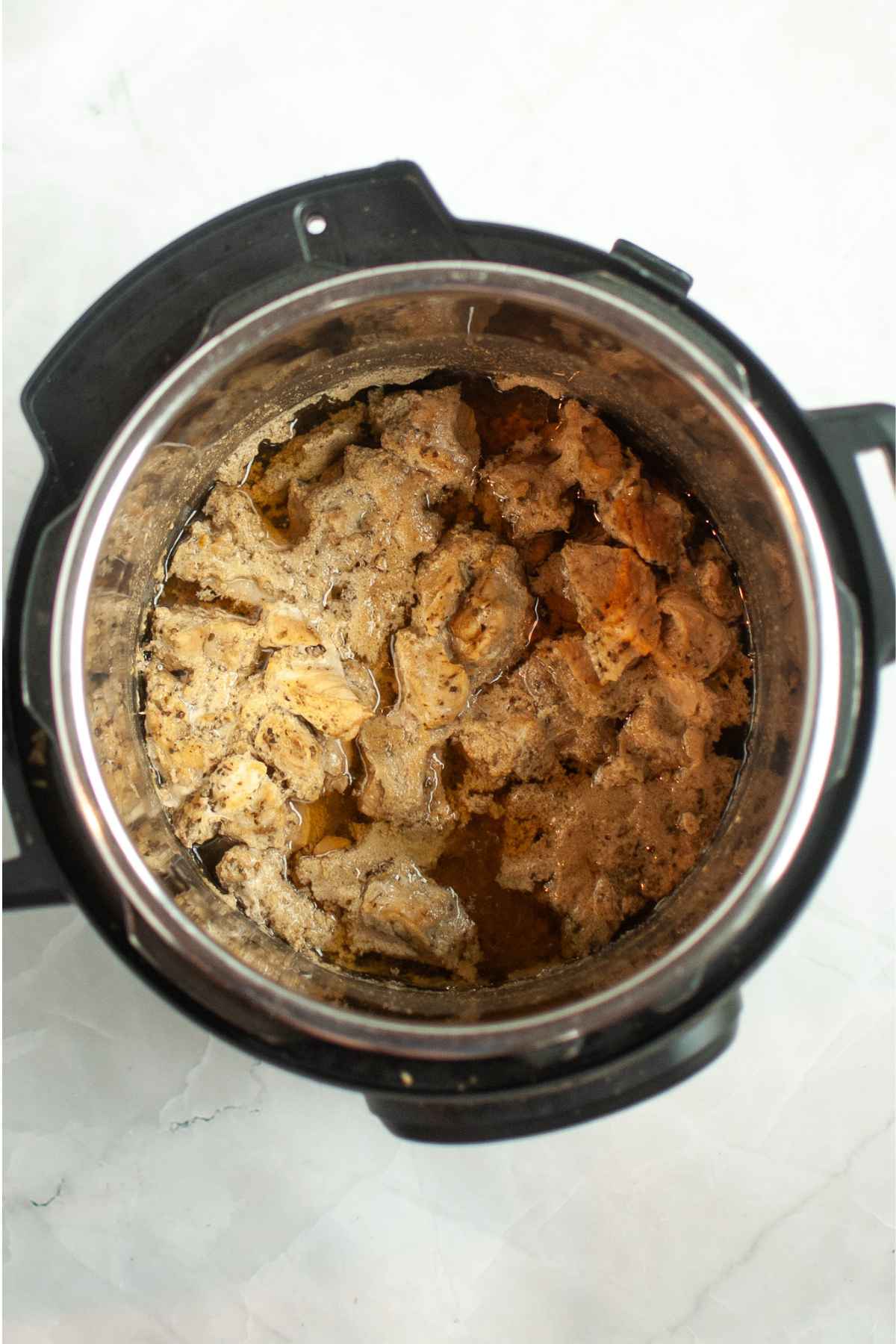 Cooked chunks of pork shoulder simmering in broth inside a stainless steel Instant Pot.