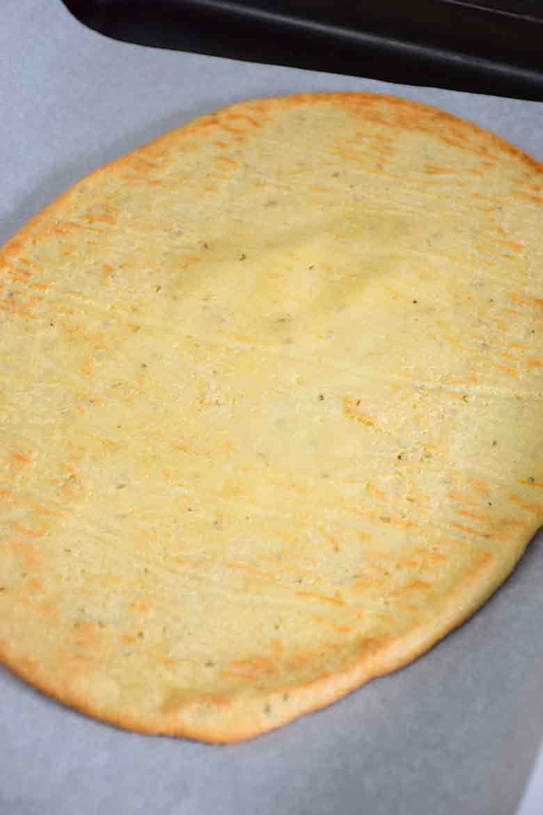 Baked keto pizza crust on a parchment lined baking sheet, golden brown and slightly crisp around the edges.