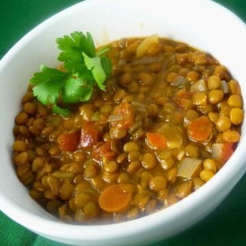 A white bowl filled with lentil stew containing chunks of tomatoes, carrots, onions, and lentils.