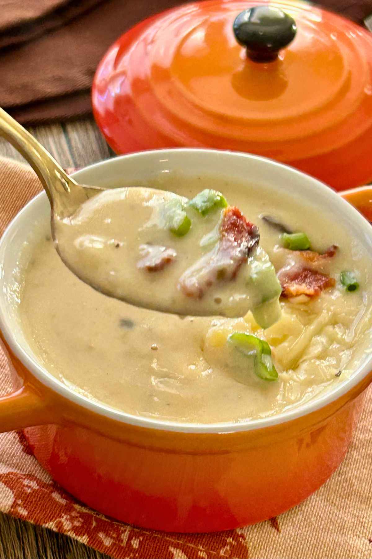 Spoonful of bacon potato soup lifted from an orange bowl.