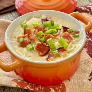 Creamy loaded potato soup served in an orange soup crock, topped with crispy bacon pieces, shredded cheese and sliced green onions.
