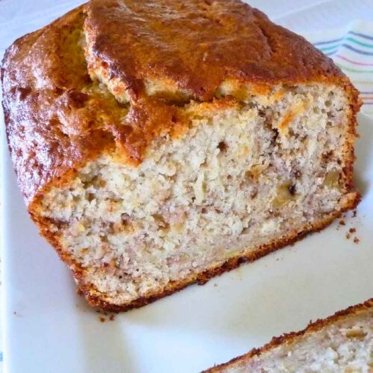 A close up of a loaf of banana bread with a golden brown crust and a tender interior speckled with bits of banana and nuts.