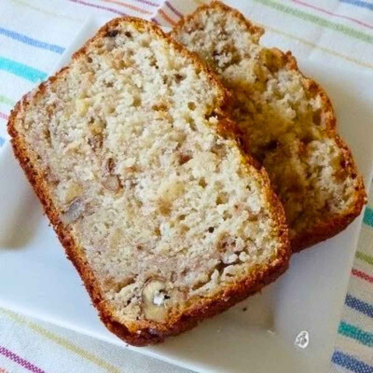 two thick slices of low fat banana bread on a white plate, revealing a moist crumb filled with chopped nuts and banana pieces.