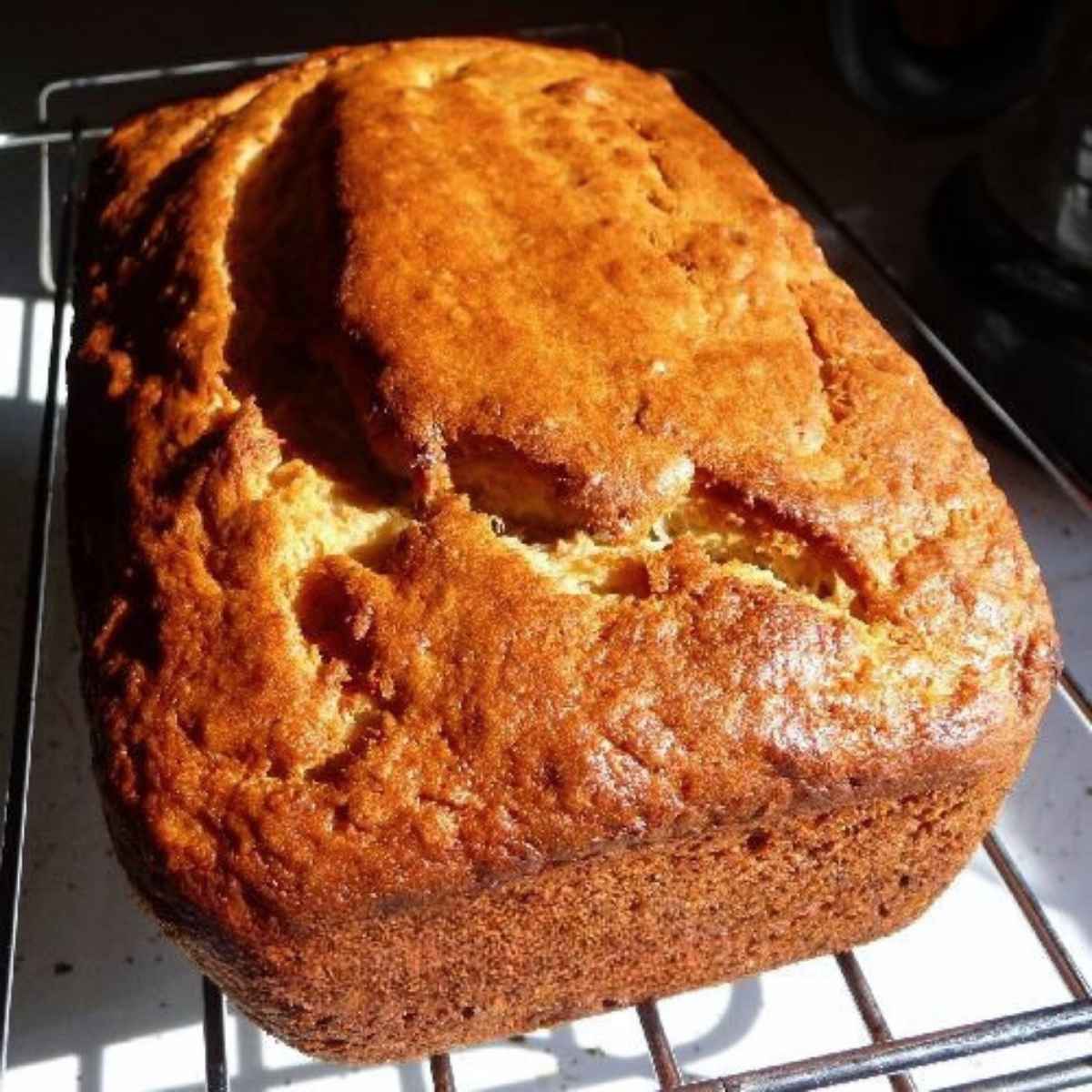 A whole loaf of freshly baked yogurt banana bread resting on a wire cooling rack, sowing a rich golden top with natural cracks and soft texture.