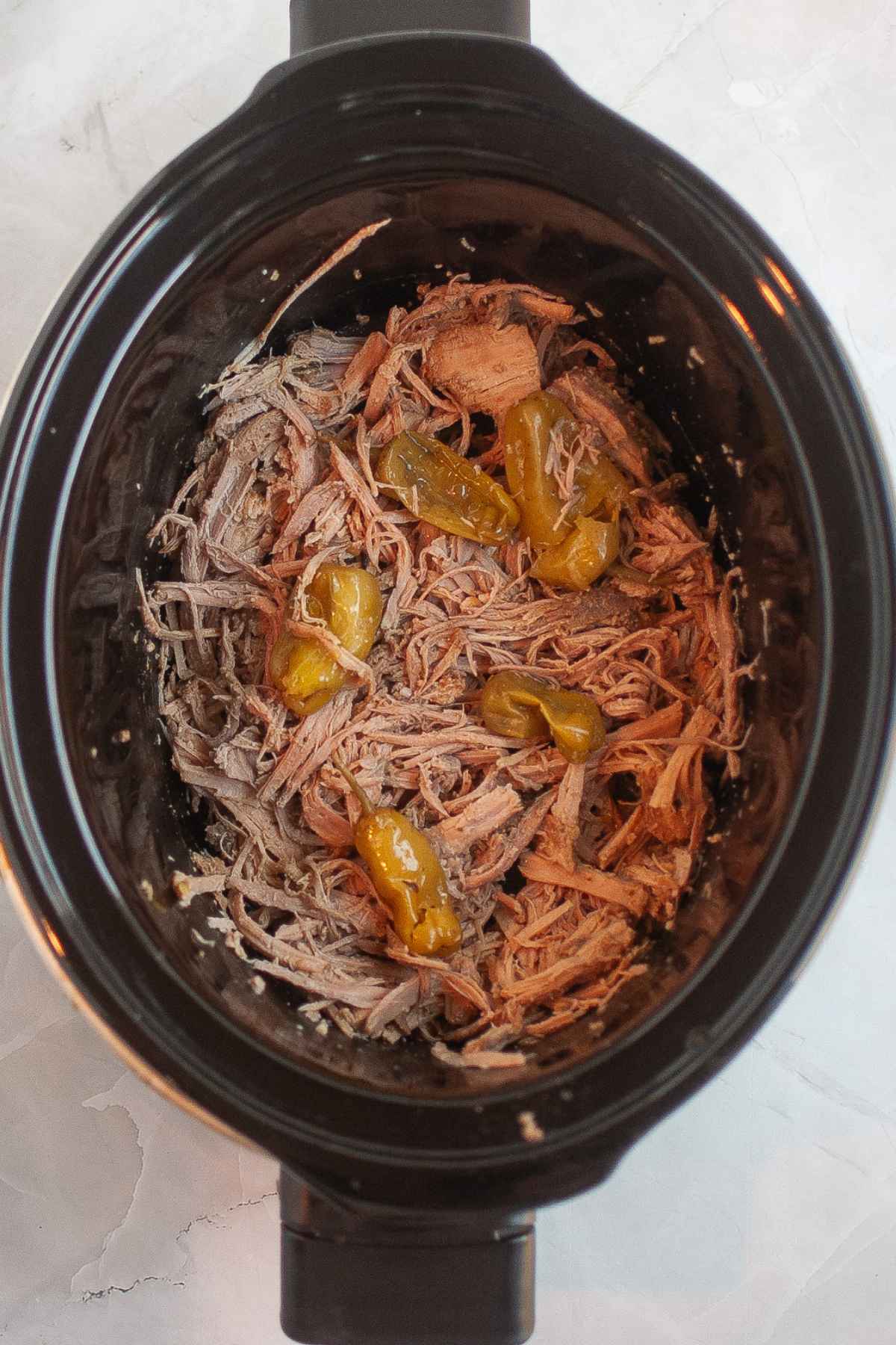 Shredded Mississippi Pork Roast mixed with pepperoncini peppers inside a slow cooker after cooking.
