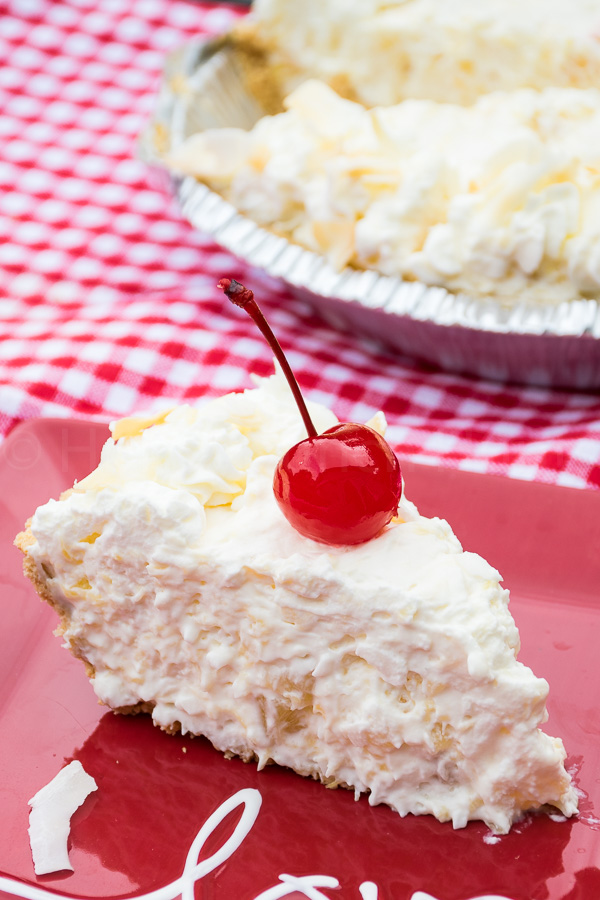 A slice of creamy tropical pie on a red plate with the word "love" garnished with a bright maraschino cherry and topped with whipped cream and coconut flakes.