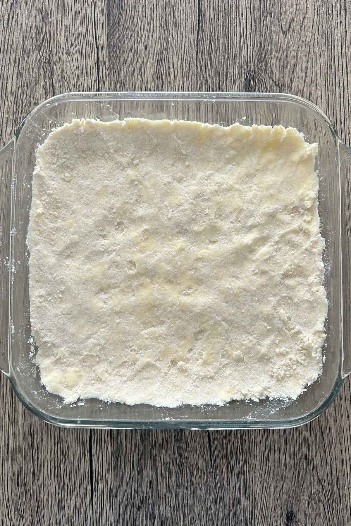 Overhead view of a glass baking dish filled with an unbaked shortbread crust pressed evenly across the bottom, ready for the pumpkin filling.