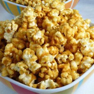 A close up of a white bowl filled with golden spicy caramel corn, each popcorn kernel coated in a shiny, crisp caramel glaze.