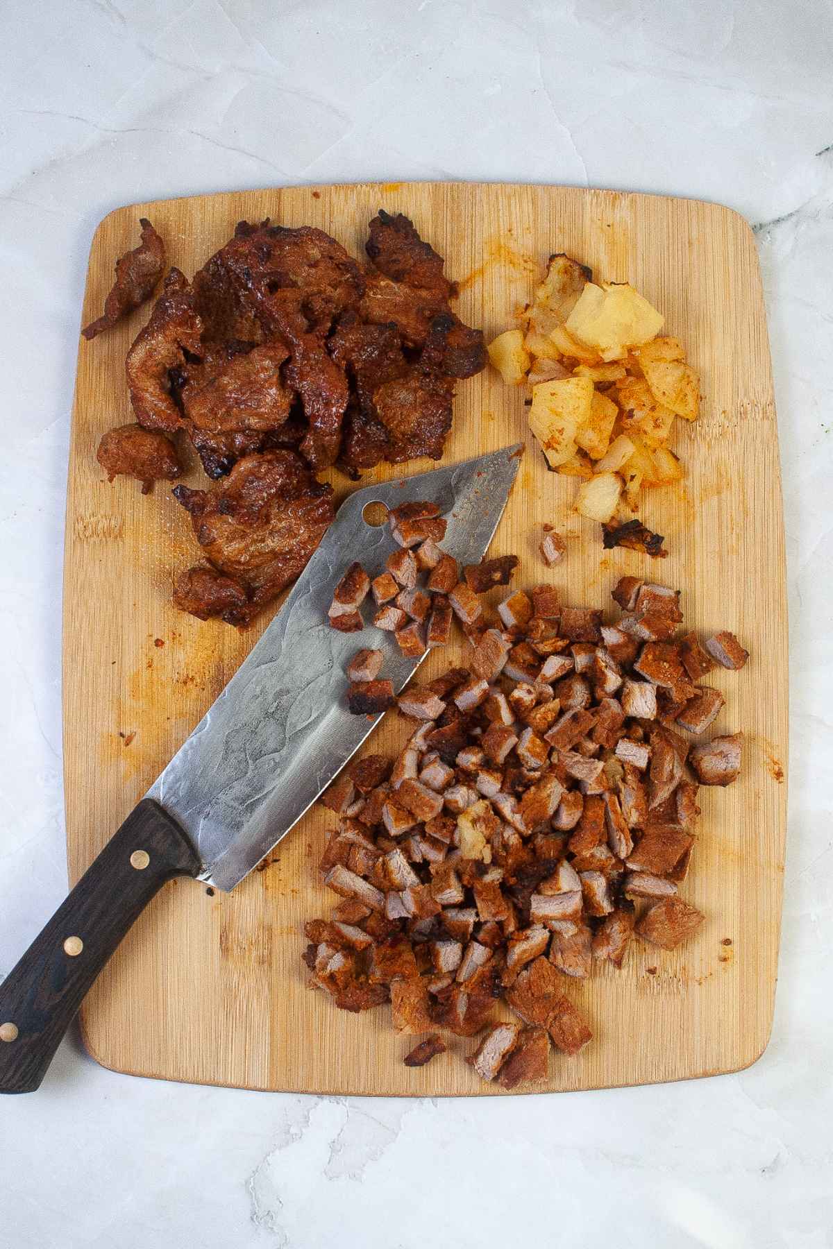 Overhead view of cooked pork and pineapple on a cutting board, with part of the pork chopped into small pieces beside a knife.