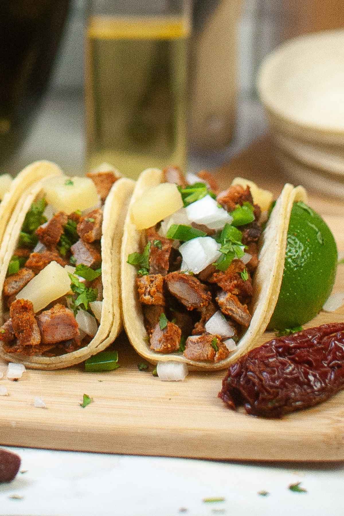 Air fryer pork tacos al pastor in corn tortillas on a wooden board topped with onion and cilantro.
