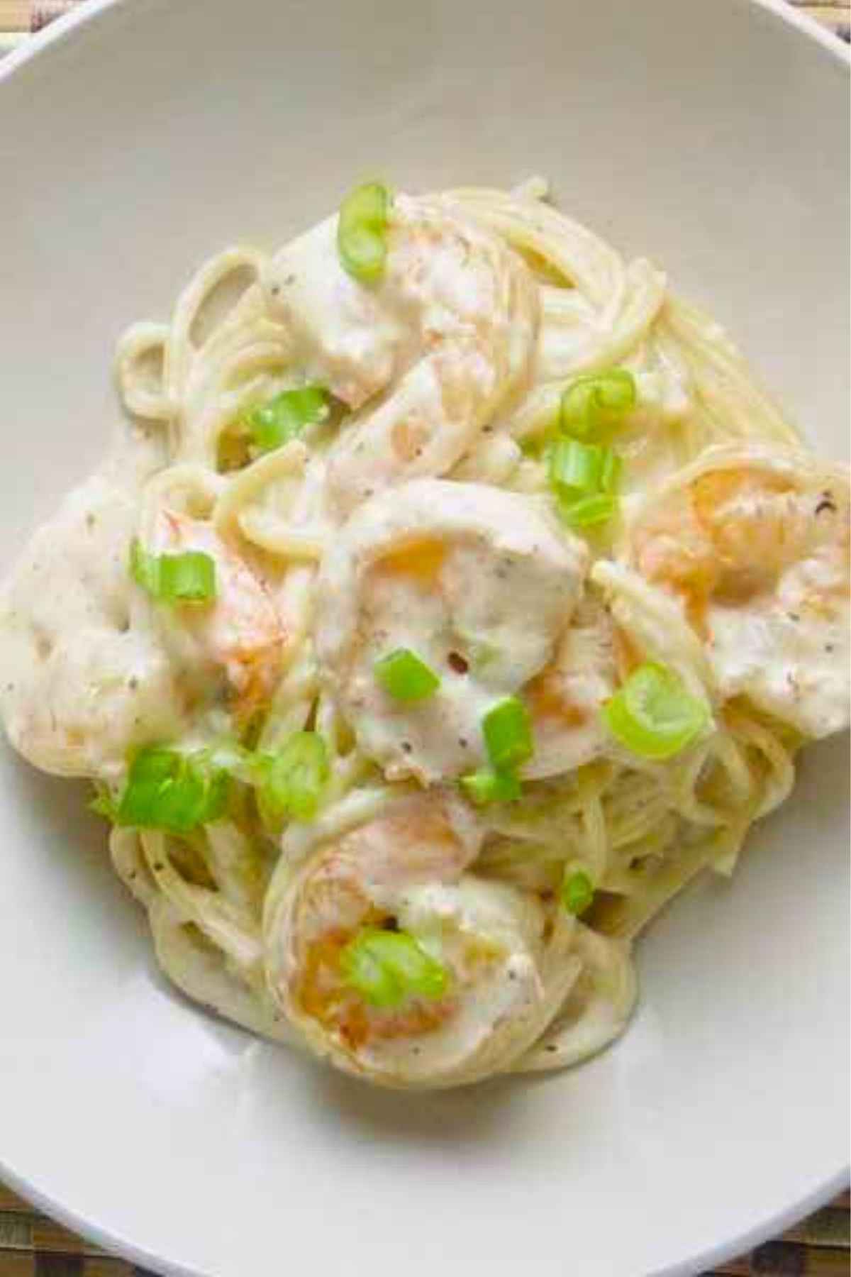 Overhead view of old bay shrimp linguine in a creamy white sauce, garnished with fresh green onion slices.