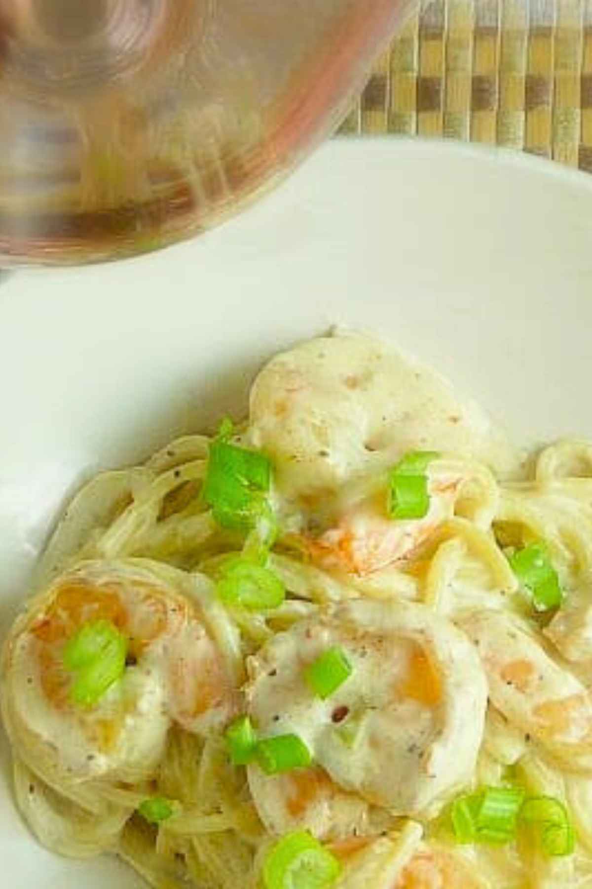 Overhead image of a bowl of creamy shrimp pasta dish garnished with green onions.