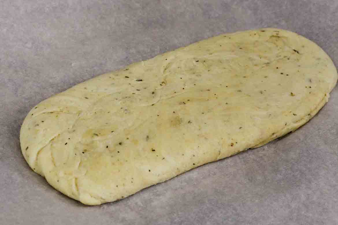 Unbaked low carb pizza dough shaped into an oval on parchment paper, ready for rolling or baking.