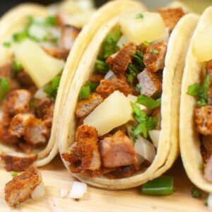 Up close image of Air fryer pork tacos al pastor in corn tortillas on a wooden board topped with onion and cilantro.