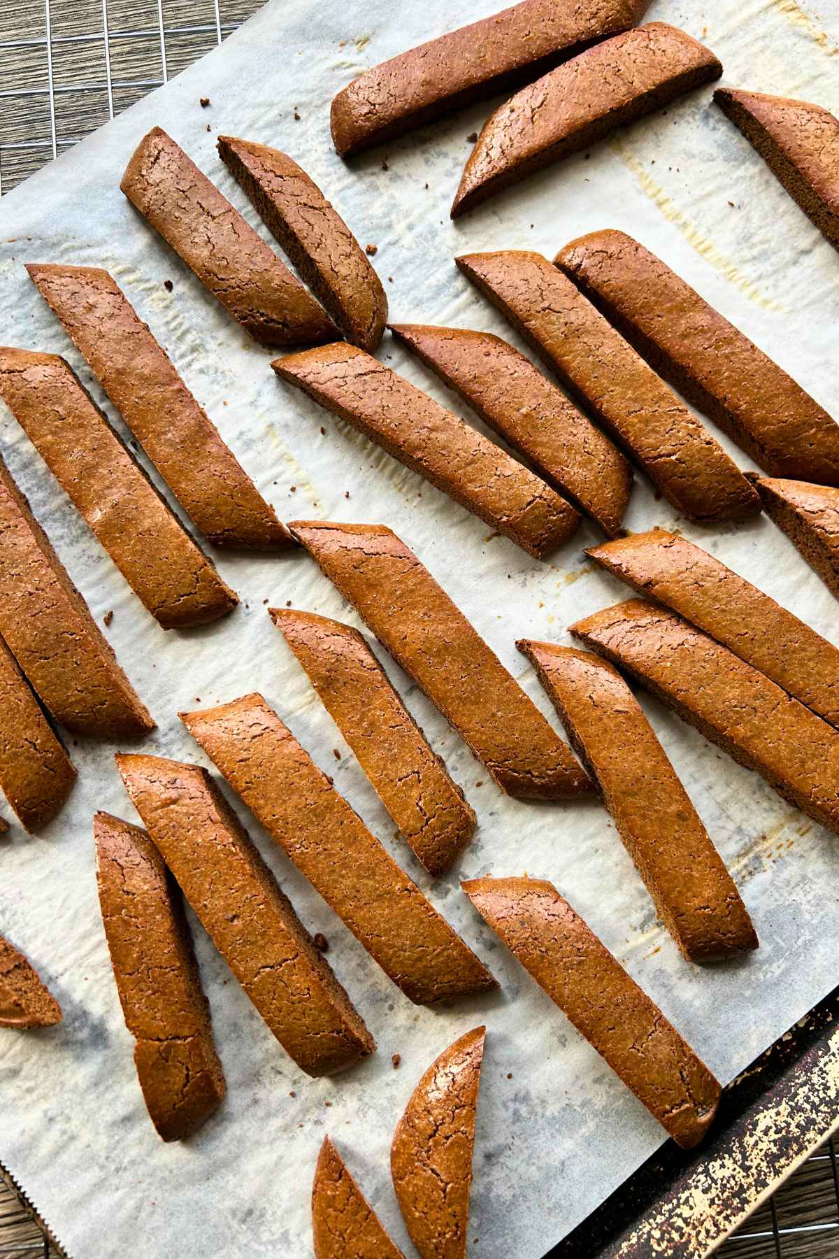 Golden brown baileys biscotti slices arranged on a parchment lined baking sheet, showing their crisp edges and slightly cracked topps after the second bake.