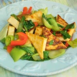 Triangle cut pies of crispy golden brown tofu mixed with sok choy and red bell pepper on a seashell blue plate.