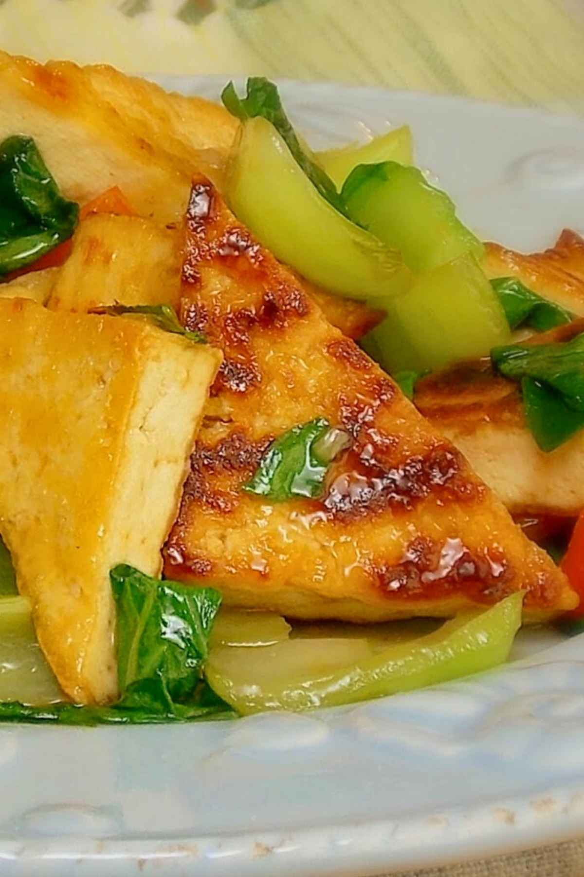 Upclose image of crispy brown tofu triangles coated in a sauce.