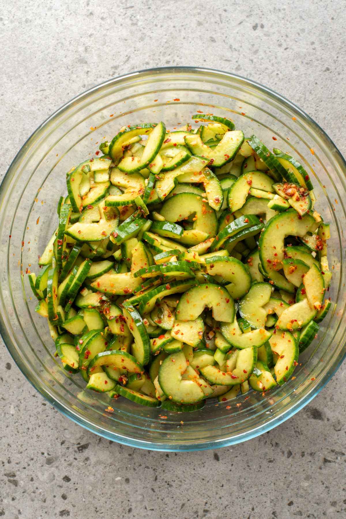 A large glass bowl filled with sliced and seeded cucumbers seasoned with a spicy viniagrette.