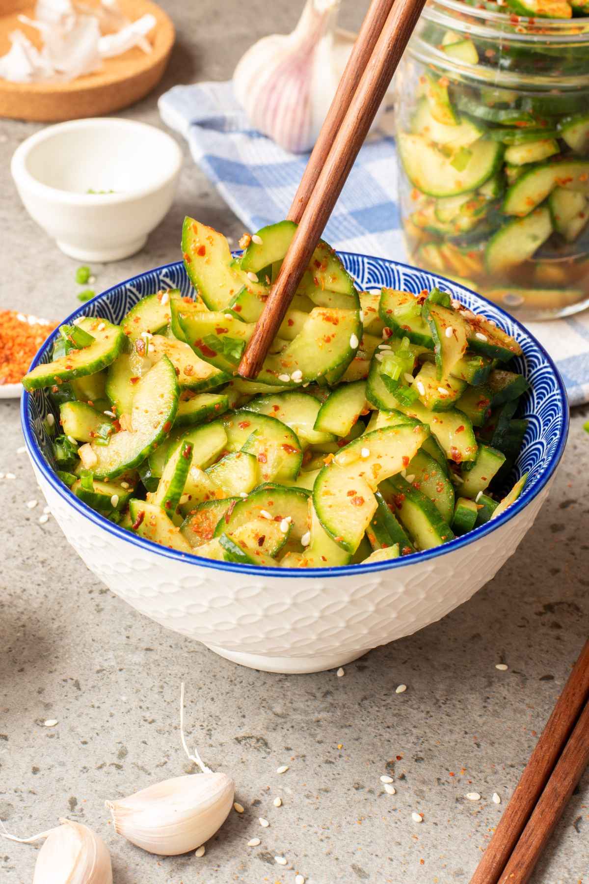 A white bowl with blue design filled with cucumber kimchi with a pair of chopsticks picking up some pieces of cucumber.