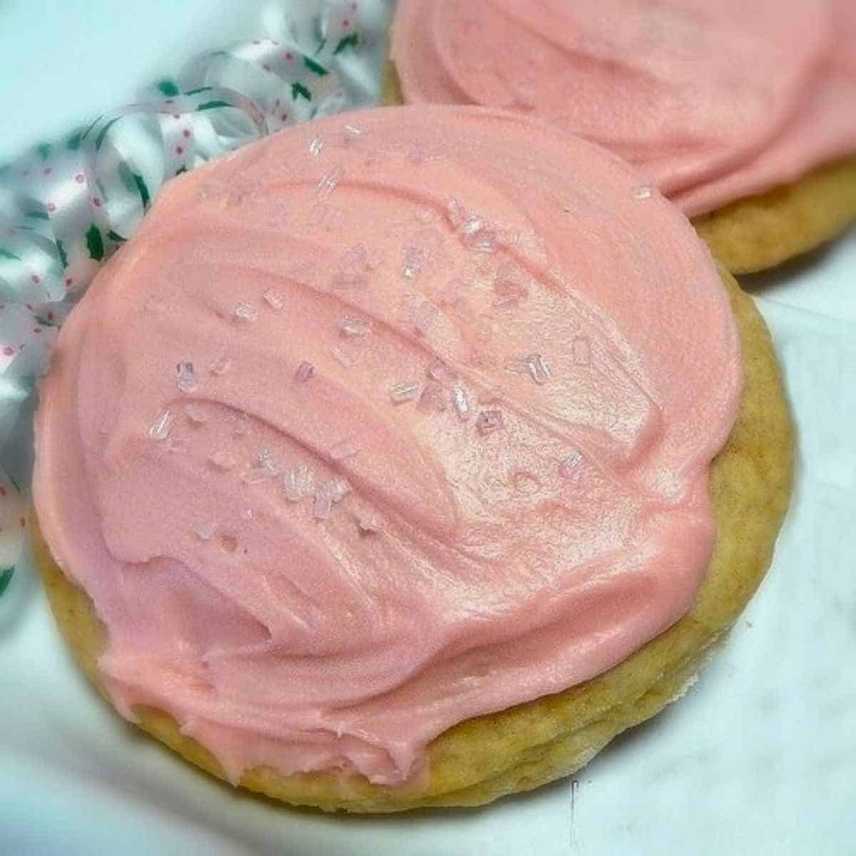 Two pink frosted craisins filled cookies on a white tray.